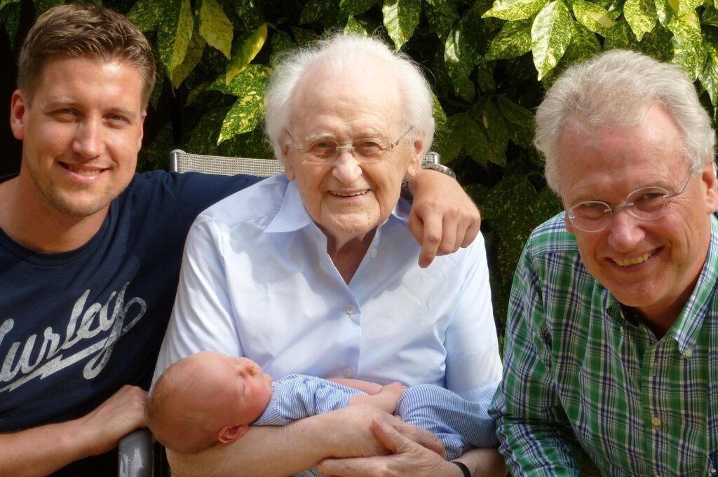 Mehrgenerationen - Baby, Vater, Großvater und Urgroßvater sitzen zusammen